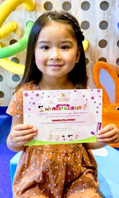 Girl holding her first haircut certificate